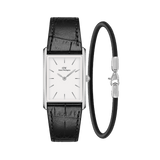 Rectangular Daniel Wellington watch with a white dial, polished silver case, and black crocodile-embossed leather strap, paired with a slim black and silver Sheffield bracelet.