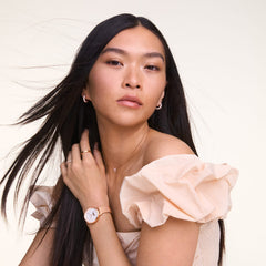 A woman wearing Pavé Crystal Earrings in rose gold, styled with matching rose gold jewellery and a soft off-the-shoulder dress.