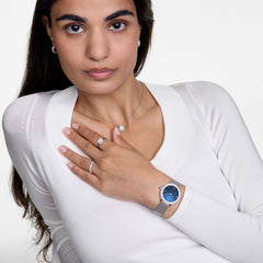Woman wearing Crystalline Bezel Sterling Blue watch with silver mesh strap and blue dial, styled with matching jewellery.