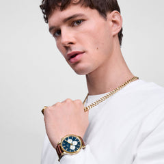 Man wearing the Ellipse Cuban Chain Necklace Gold, styled over a white top and paired with a gold watch and ring, highlighting the necklace’s bold, polished links and contemporary design.