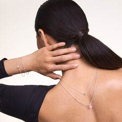 A woman wears a silver necklace featuring the Charm Heart Crystal Pink Silver, a heart-shaped pink crystal pendant, styled with matching silver jewellery for an elegant look.