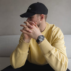 Man wearing the Classic Mesh Graphite watch with a graphite sunray dial and mesh strap, styled casually with a yellow jumper and black cap.