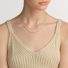 A woman wears a delicate flat chain rose gold necklace layered elegantly over a cream knitted top.