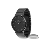 Sleek Daniel Wellington black steel link watch with a minimalist black dial, paired with a polished silver-tone ring engraved with the brand’s signature, presented as a coordinated gift set.