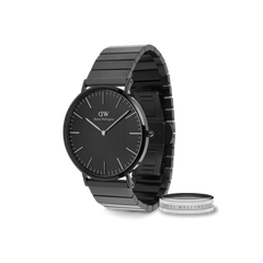 Sleek Daniel Wellington black steel link watch with a minimalist black dial, paired with a polished silver-tone ring engraved with the brand’s signature, presented as a coordinated gift set.