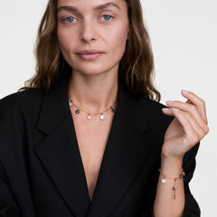 Woman wearing a gold chain necklace featuring the Blue Spot Oval Gold Charm alongside other colourful charms, styled with a matching gold charm bracelet and a black blazer for an elegant, modern look.