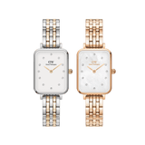 Two Daniel Wellington Quadro Lumine women’s watches, one in a gold and silver two-tone finish with a white dial, the other in rose gold with a mother of pearl dial, both featuring rectangular faces, crystal hour markers, and five-link metal bracelets.
