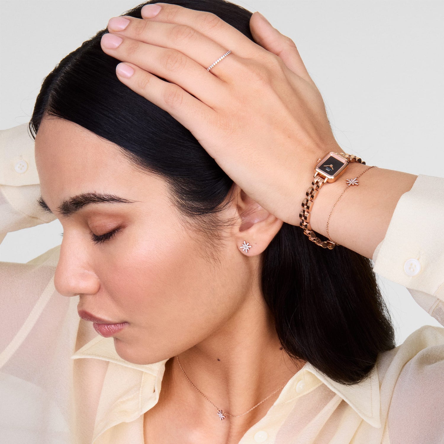 Woman wearing the Mirelle Star Necklace Rose Gold, styled with matching star-shaped earrings, a rose gold watch, and bracelet, showcasing the necklace’s delicate chain and sparkling star pendant against a light blouse.