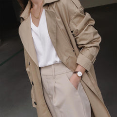 Woman wearing Daniel Wellington Petite St Mawes Rose Gold watch with brown leather strap, styled with a beige trench coat.