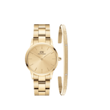 Gold Daniel Wellington watch with a minimalist dial and matching gold link strap, paired alongside a slender gold cuff bracelet featuring subtle crystal accents and engraved branding.