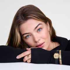 A woman wearing the Classic Bangle Gold by Daniel Wellington on her wrist, styled alongside a gold watch and black strap for a sophisticated, layered look.