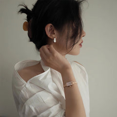 A woman wearing the Quadro Mini Melrose Blush watch with a blush pink rectangular dial and rose gold mesh strap, styled with a white blouse for an elegant, minimalist look.