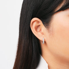 A petite pavé crystal silver hoop earring with a rounded profile is worn on the ear, showcasing its sparkling cubic zirconia and elegant, modern design.
