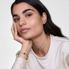 A woman wears the Mother of Pearl Octagon Rose Gold Charm on a delicate chain necklace, styled with other gold jewellery for a layered, elegant look. The iridescent mother of pearl charm stands out against her light top, adding a refined touch to her outfit.