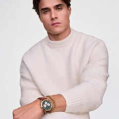 A person wearing the Ellipse Cuban Chain Bracelet Gold alongside a watch, styled with a cream knit jumper for a modern, polished look. The gold bracelet’s substantial links and lustrous finish complement the outfit and watch, highlighting its versatility for everyday wear.