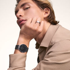 Man wearing the Classic Piano Link Onyx Silver watch by Daniel Wellington, featuring a brushed black dial and silver piano link strap, styled with a beige shirt for a refined, modern look.