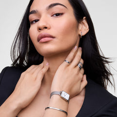 A woman wearing the Classic Aura Ring Silver by Daniel Wellington, styled with other silver jewellery including a watch, bangle, and hoop earring, showcasing the ring’s row of white cubic zirconia crystals and engraved band for a refined, modern look.