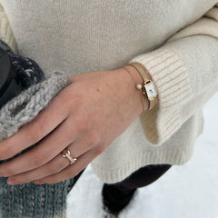 A woman wearing the Quadro Mini & Pavé Crystal Gold Set, featuring a petite rectangular gold watch with a white dial and a delicate gold bracelet with a pavé crystal charm, styled with a cosy cream jumper in a winter outdoor setting.