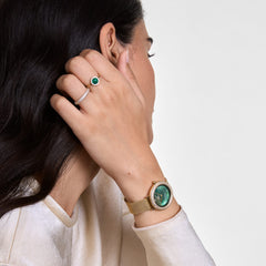 Woman wearing the Crystalline Bezel & Audrey Green Set Gold, featuring a gold mesh strap watch with an emerald green dial and crystal bezel, paired with a matching gold ring set with a green stone and delicate crystals.