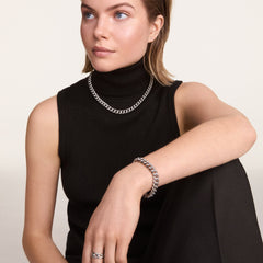 A person wearing the Chunky Chain Bracelet Silver on their wrist, styled with a matching silver chain necklace and ring, paired with a sleeveless black top for a modern, sophisticated look.