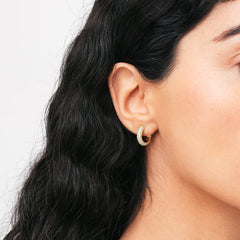 A gold pavé crystal hoop earring with sparkling cubic zirconia stones is worn on the ear, showcasing its elegant and refined design.
