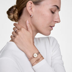 Woman wearing the Classic Unity Lumine rose gold bracelet with intertwined rings and crystals, styled alongside a matching rose gold watch and minimalist jewellery.