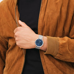 A man wearing the Classic Multi-Eye Sterling Arctic watch with a blue multi-eye dial and silver mesh strap, styled with a tan suede jacket and black shirt.