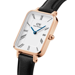 Close-up of the Quadro Roman Numerals Sheffield Rose Gold watch featuring a rectangular rose gold case, white dial with black Roman numerals, blue steel hands, and a black leather strap.