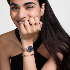 Woman wearing Daniel Wellington Petite Melrose watch with black dial and rose gold mesh strap, styled with a matching bracelet.