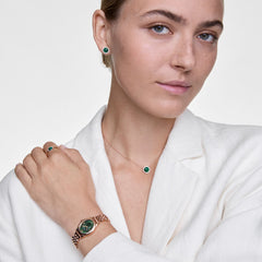 Woman wearing the Ophelia Mini Emerald Rose Gold watch with a polished rose gold beans link bracelet and emerald green oval dial, styled with matching emerald jewellery and a white blazer for an elegant, coordinated look.