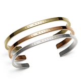 Set of three Daniel Wellington cuff bracelets in polished gold, rose gold, and silver finishes, each featuring a minimalist design with engraved branding. The trio is elegantly stacked, showcasing their refined curves and versatile metallic tones.