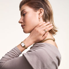 Woman wearing Quadro Pressed Evergold gold mesh watch with rectangular dial, styled with gold jewellery and a neutral top.