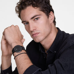 A man wearing the Classic Mesh Onyx Black watch with a black sunray dial and stainless steel mesh strap, styled with a dark shirt for a modern, minimalist look.