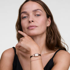 Woman wearing a Classic Tennis Bracelet Apricot Gold on her wrist, styled alongside a gold watch and a black sleeveless top, highlighting the delicate apricot-coloured crystals and elegant, stackable design.
