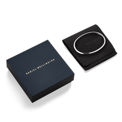 Daniel Wellington Classic Bangle Silver displayed on a black pouch next to an elegant navy gift box, highlighting its polished stainless steel finish and refined presentation, ideal for gifting.