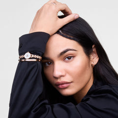 A person wearing the Classic Lumine Bracelet Rose Gold 55mm on their wrist, styled with a matching rose gold watch and a black long-sleeve shirt, showcasing the bracelet’s polished finish and sparkling cubic zirconia crystals.