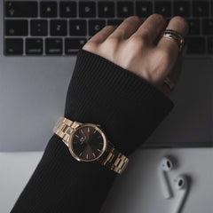 A person wearing the Daniel Wellington Iconic Link Amber watch with a rose gold bracelet and brown sunray dial while working at a laptop.