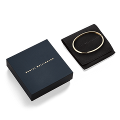 Classic Bangle Gold by Daniel Wellington displayed with its elegant black pouch and navy gift box, highlighting refined packaging and polished gold finish.
