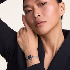Woman wearing Quadro Mini Crystal Zodiac Sterling watch with silver mesh strap, black dial, and sparkling zodiac charm.