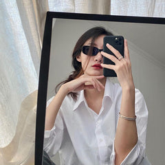 Woman wearing the Emalie Ring Satin White Rose Gold on her finger, styled with a matching rose gold bangle and a crisp white shirt in a modern, casual setting.
