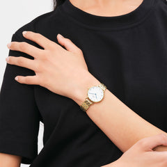 Woman wearing a petite gold 5-link Roman numeral watch with white dial and blue hands, styled with a black top.