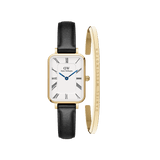 Rectangular gold Daniel Wellington watch with a white Roman numeral dial, blue hands, and black leather strap, paired with a slim gold bracelet engraved with the brand’s signature.