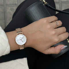 Petite Lumine 5 Link Melrose White MoP Rose Gold watch with a white mother of pearl dial and rose gold bracelet, styled on a woman's wrist with coordinating jewellery and a black handbag.