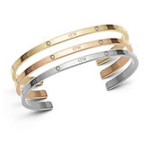 Set of three slim cuff bracelets in polished gold, rose gold, and silver finishes, each featuring subtle crystal accents and the engraved DW signature, displayed stacked together.