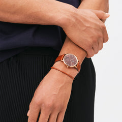 A man wearing the Classic Multi-Eye St Mawes Amber Rose Gold watch with an amber dial, rose gold case, and brown leather strap, styled with casual clothing.