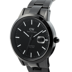 Close-up of the Daniel Wellington Iconic Link Automatic Black watch showing its glossy black enamel dial, luminous markers, magnified date window, and stainless steel bracelet.