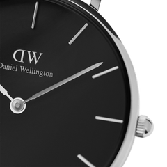 Close-up of Petite Sterling women’s watch showing black minimalist dial, silver hands, and polished stainless steel case.