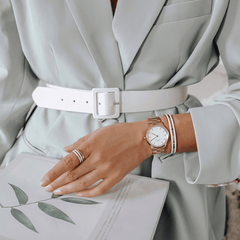 A woman wearing the Daniel Wellington Iconic Link Rose Gold watch with a polished rose gold bracelet and minimalist white dial, styled with a light suit and matching accessories.
