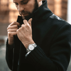Man wearing Daniel Wellington Iconic Link Silver watch with white dial and stainless steel bracelet, styled with a dark coat.