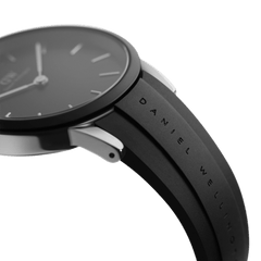 Detail view of the Daniel Wellington Iconic Motion watch showing the engraved black FKM rubber strap and minimalist black dial with silver markers.